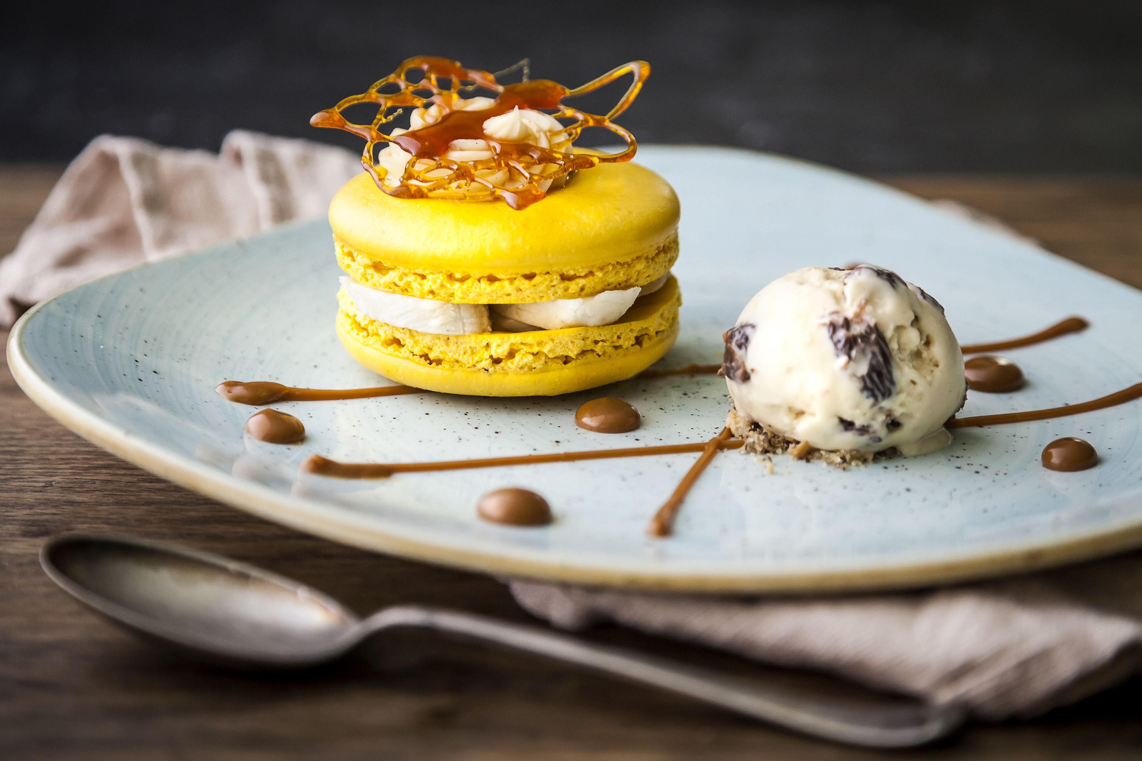 Un piatto dessert con macarons e una pallina di gelato, guarnito con salsa al caramello e noci.