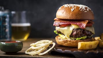 Una hamburguesa con tocino, queso y lechuga, acompañada de papas fritas y un recipiente pequeño de salsa.