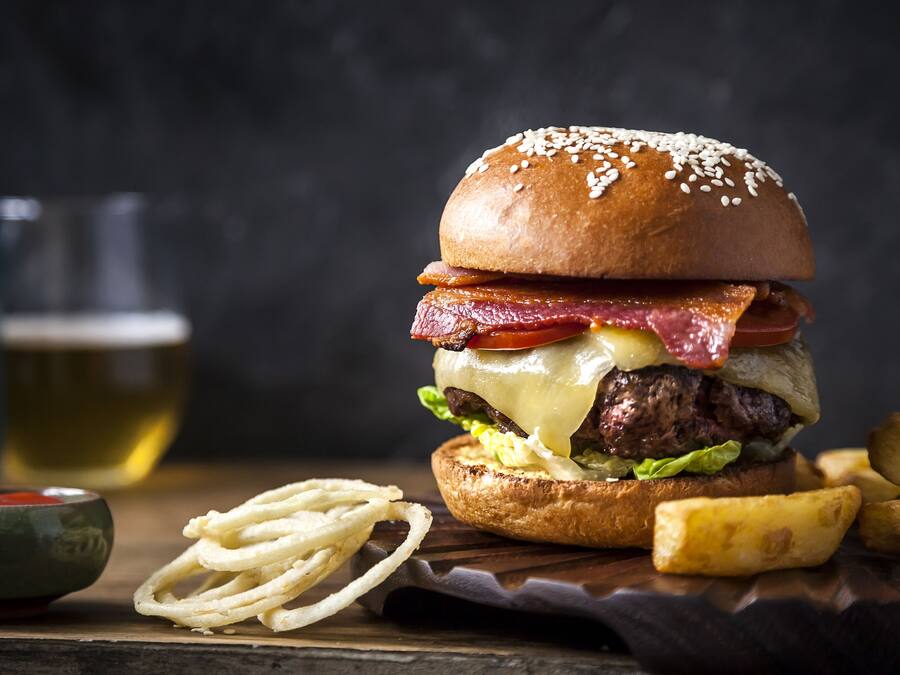 Un hamburger con bacon, formaggio e lattuga, servito con patatine fritte e una piccola ciotola di salsa.