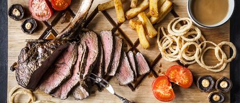 Tábua de madeira com carne fatiada, batatas fritas, anéis de cebola e tomates.