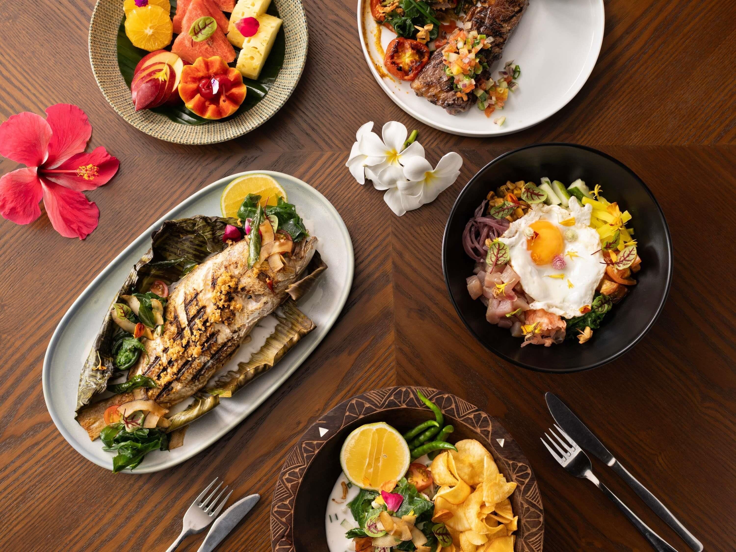 A dining table with various dishes, including grilled fish, a salad, and a plate with fruit and cheese.
