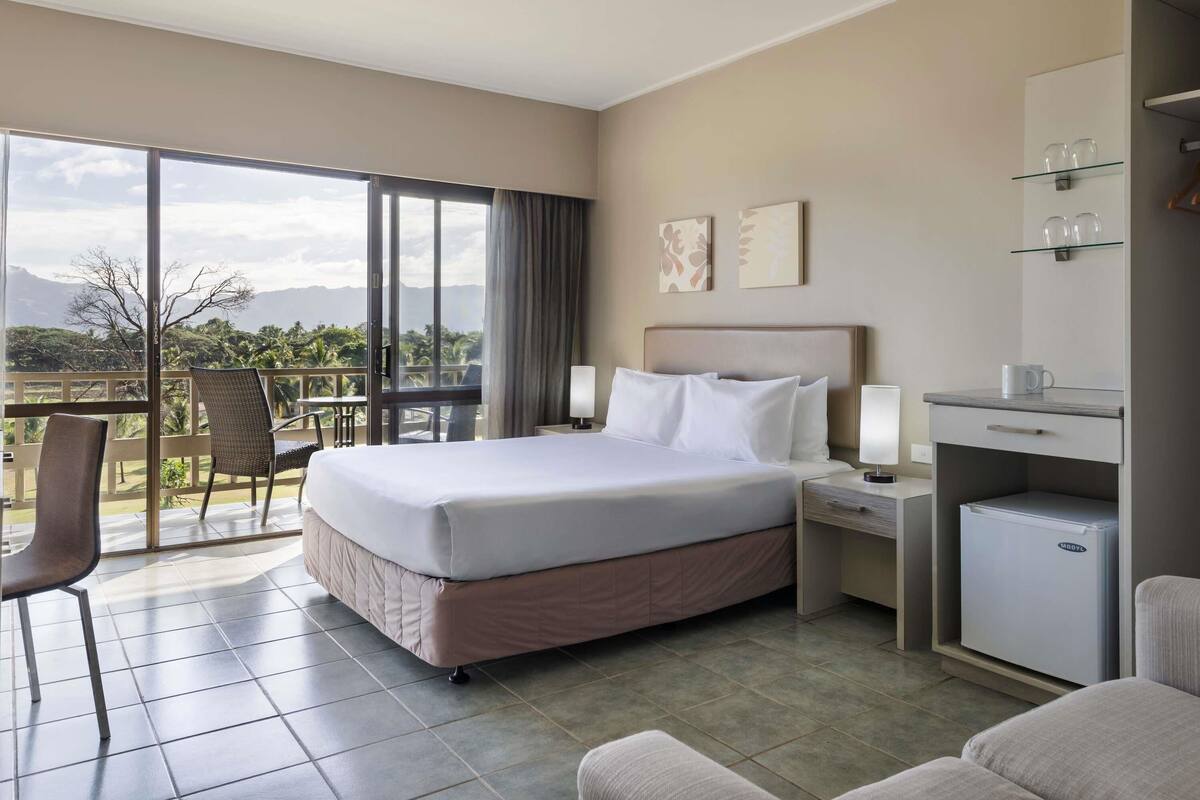 A hotel room with a bed, a desk, a chair, a minibar, and a balcony with a view.