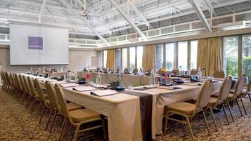 A conference room with long tables, chairs, and a projector screen displaying the Novotel logo.