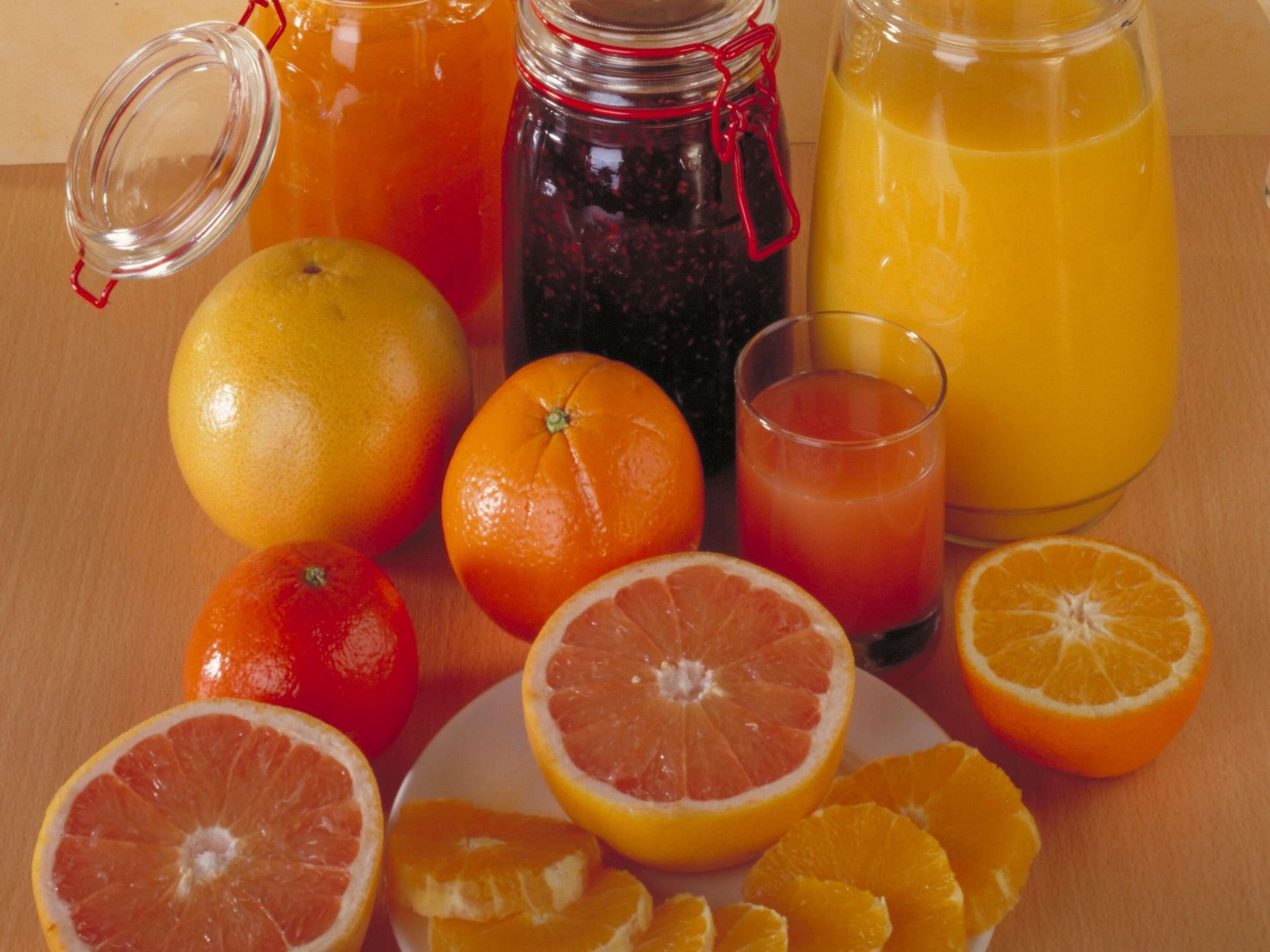 A wooden table with a variety of citrus fruits and a glass of orange juice.