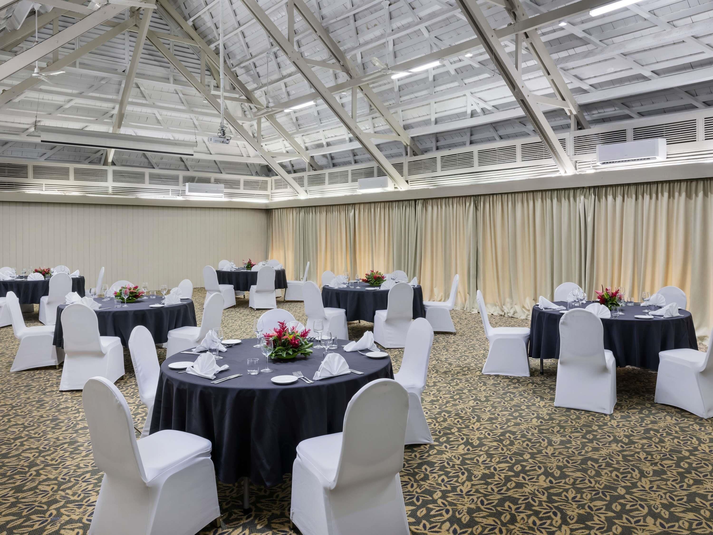 A conference room with round tables, white chairs, and black tablecloths.