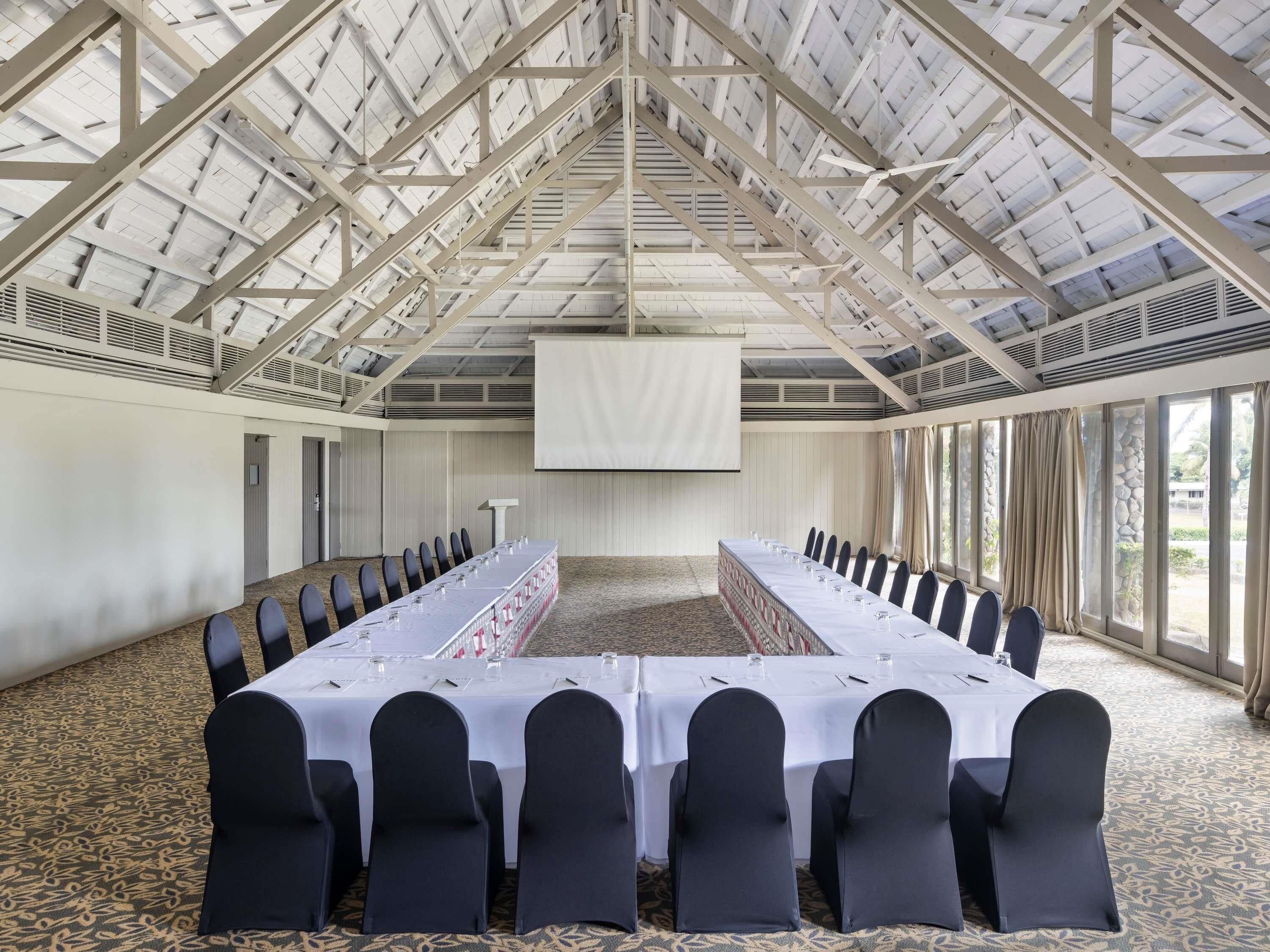 Un salón de conferencias con techo alto, mesas largas y sillas.