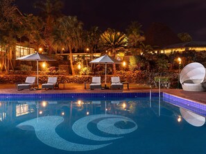 A nighttime pool area with lounge chairs and umbrellas, surrounded by palm trees and a stone wall. - Novotel Nadi (Nadi)