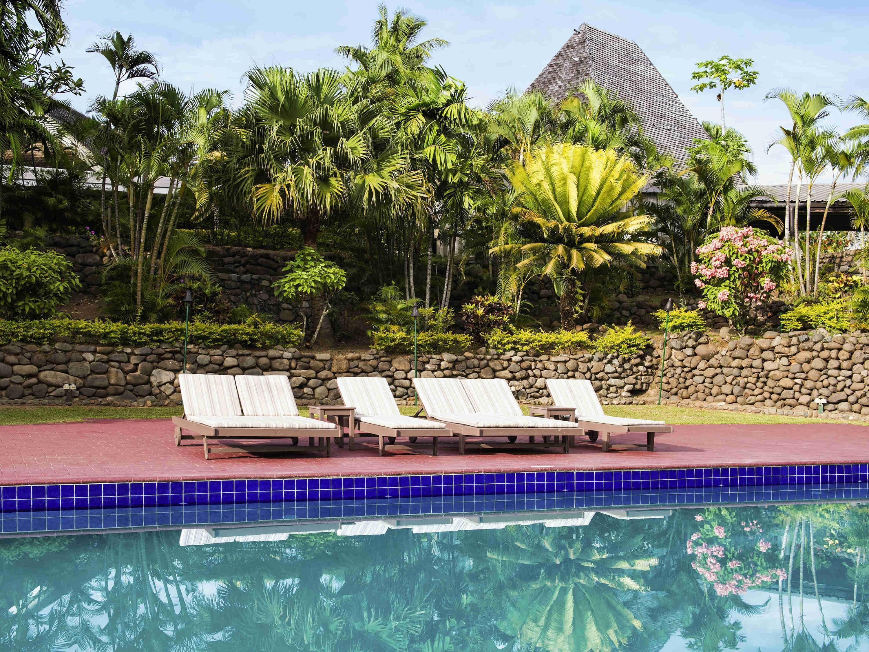 A poolside area with lounge chairs, a stone wall, and tropical vegetation.