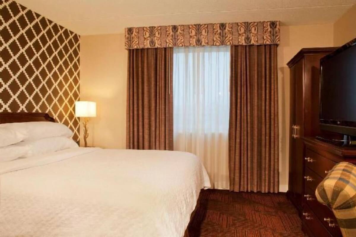A hotel room with a bed, curtains, a television, and a dresser.