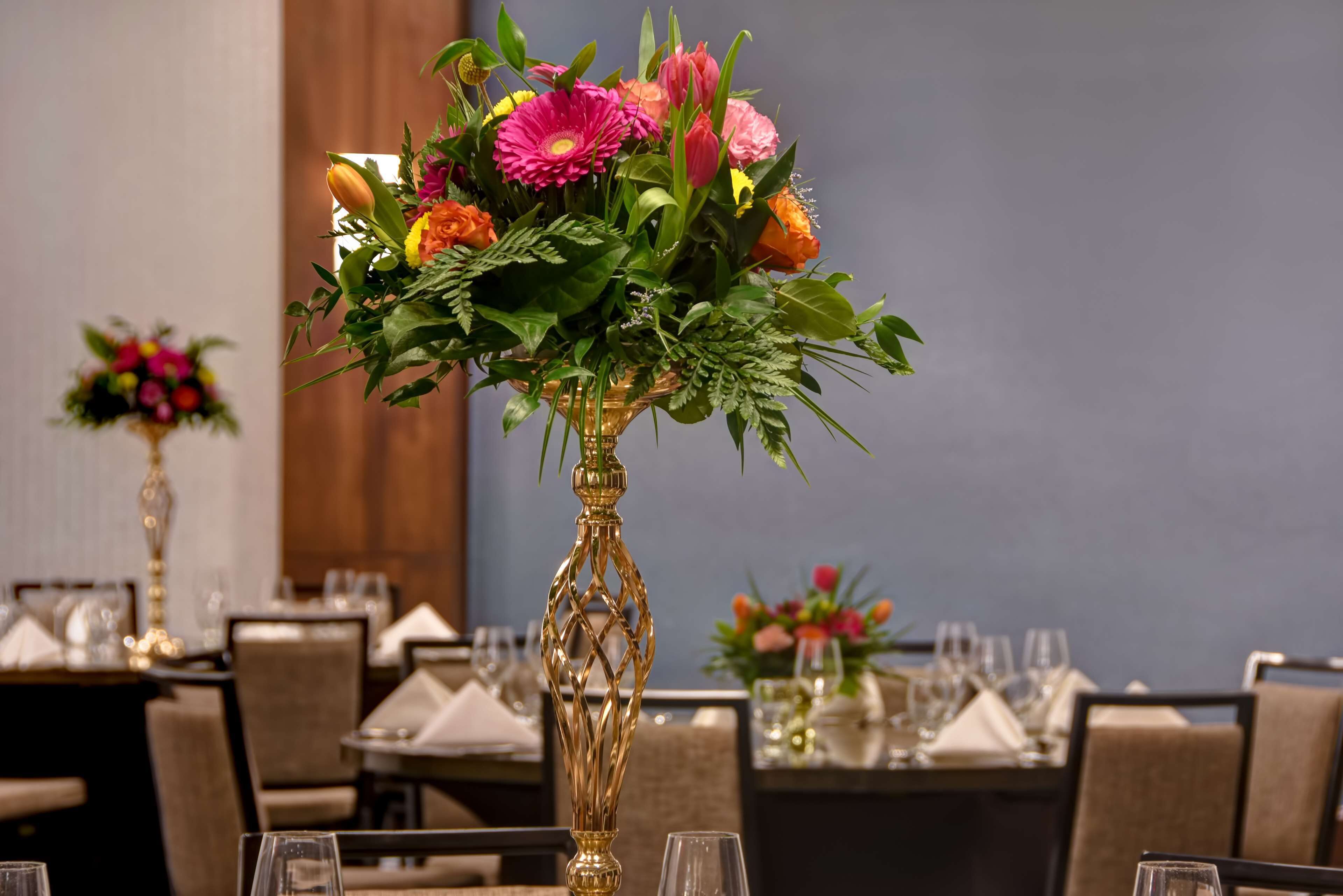 A dining table set with a gold vase of flowers, chairs, and tableware.
