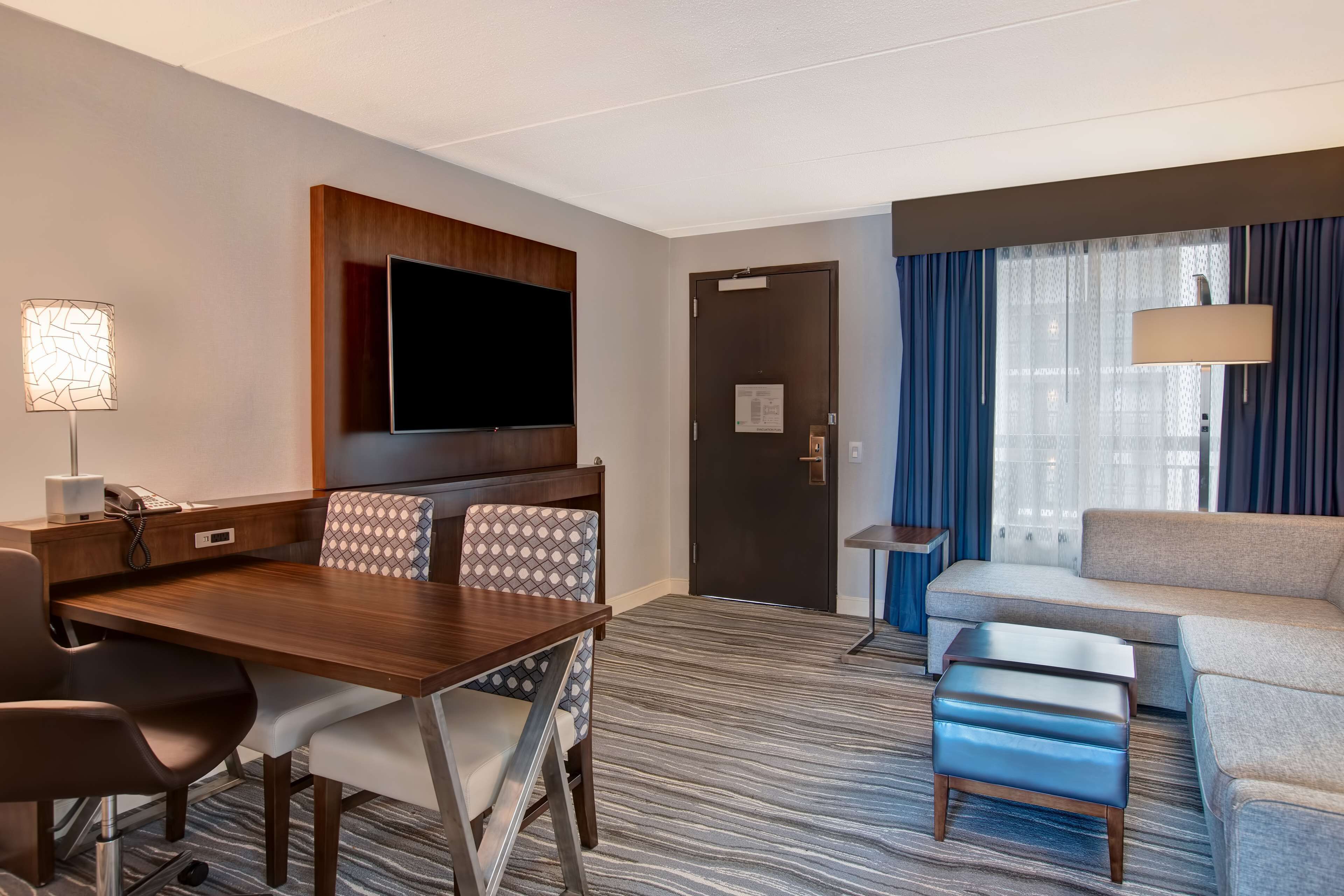 Habitación de hotel con una mesa de comedor, sillas, un sofá, un televisor, una lámpara y una puerta.