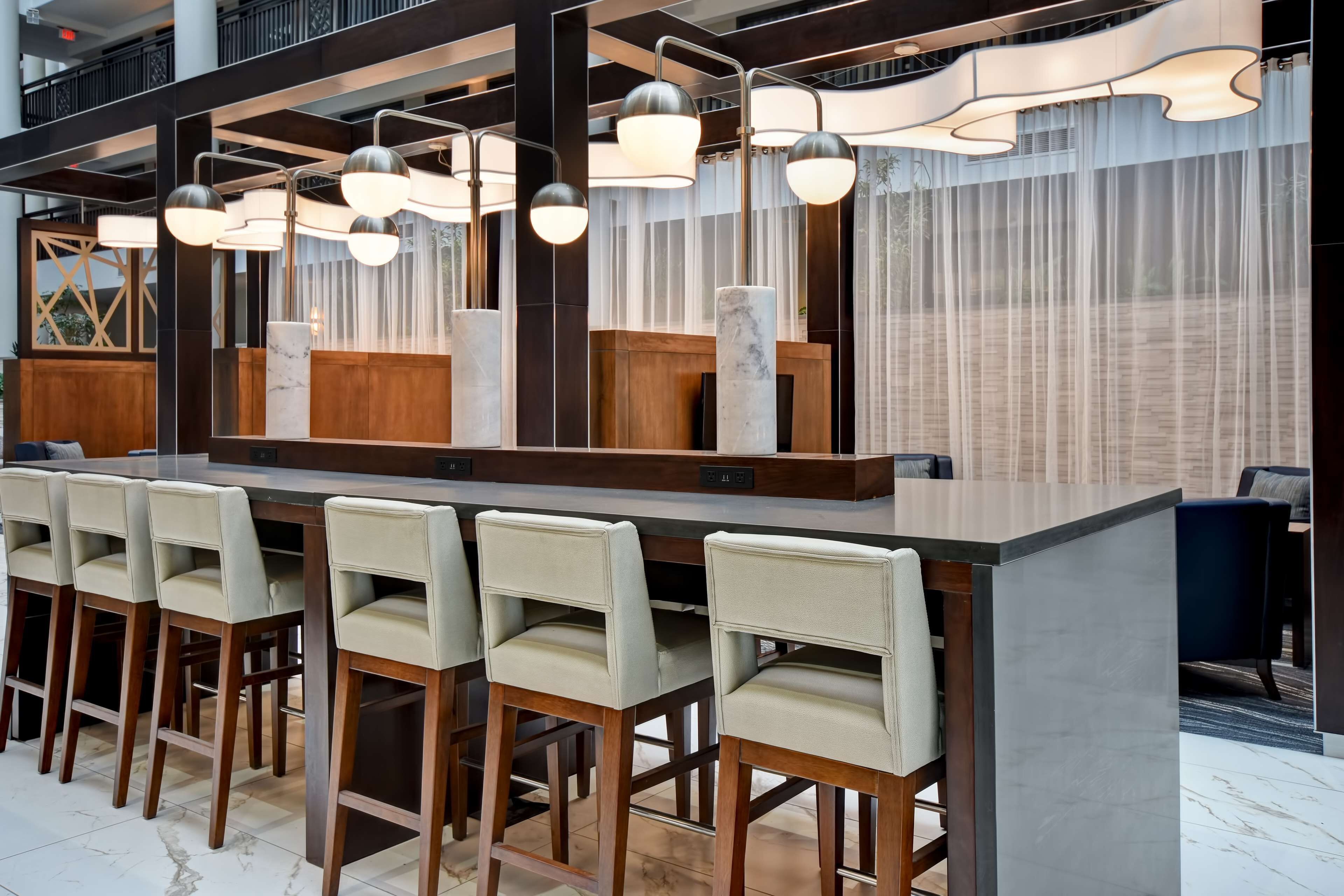 A modern bar area with a long counter, multiple bar stools, and contemporary lighting fixtures.