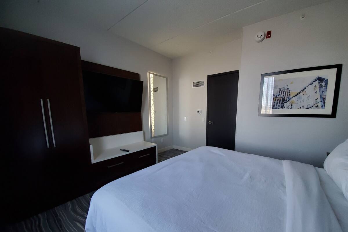 A hotel room with a large bed, a desk with a mirror, a wardrobe, and a framed picture on the wall.