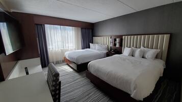 Una habitación de hotel con dos camas, televisión, escritorio y ventana con cortinas.