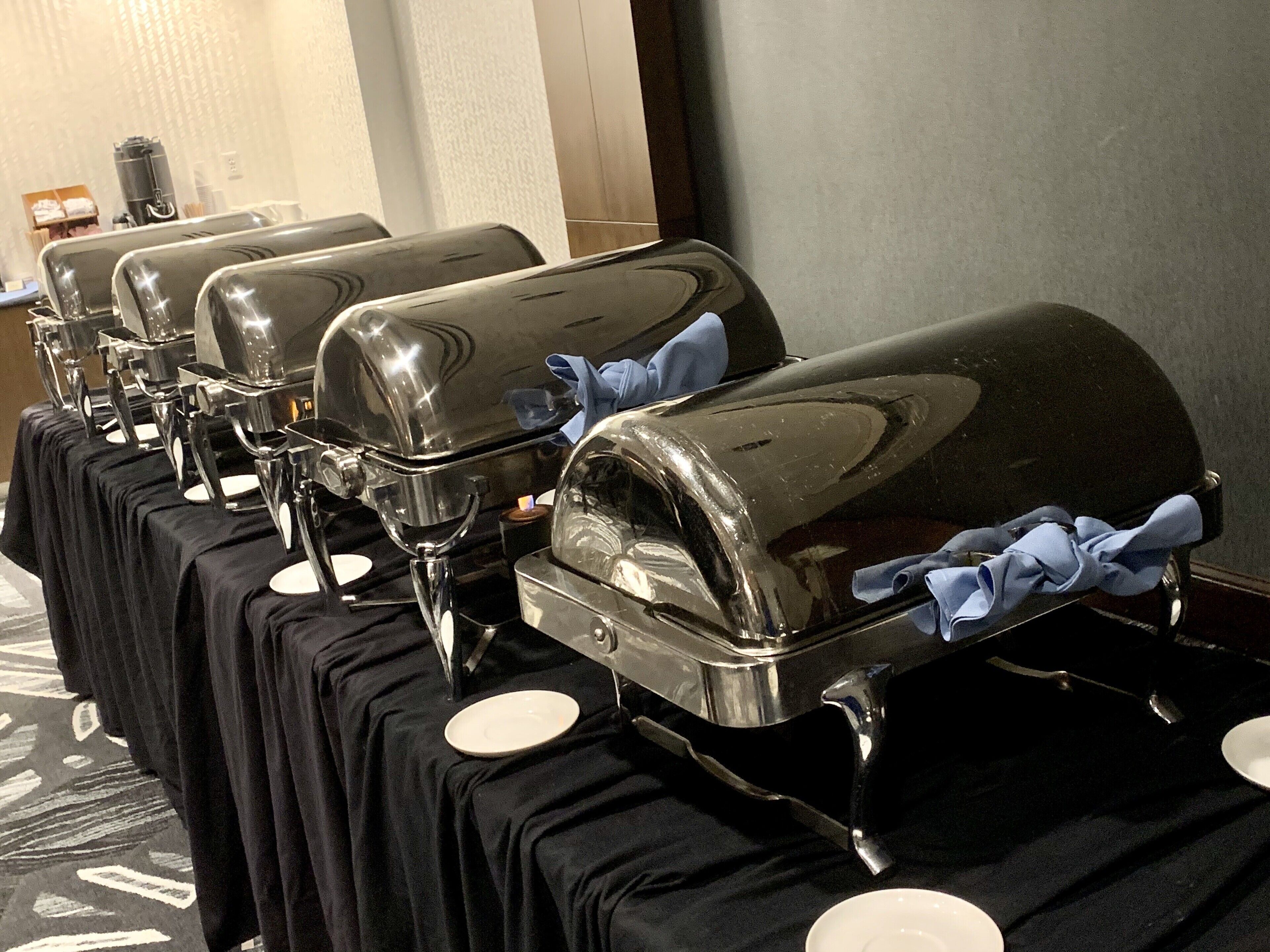 Une rangée de tables de buffet, chacune dotée d’une grille noire brillante et ornée d’un tissu bleu noué autour du manche.