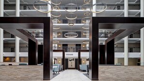 Un hall d’entrée spacieux au design moderne, doté d’un espace salon central avec des canapés et d’un plafond haut orné de luminaires circulaires.