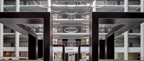 Un hall d’entrée spacieux au design moderne, doté d’un espace salon central avec des canapés et d’un plafond haut orné de luminaires circulaires.