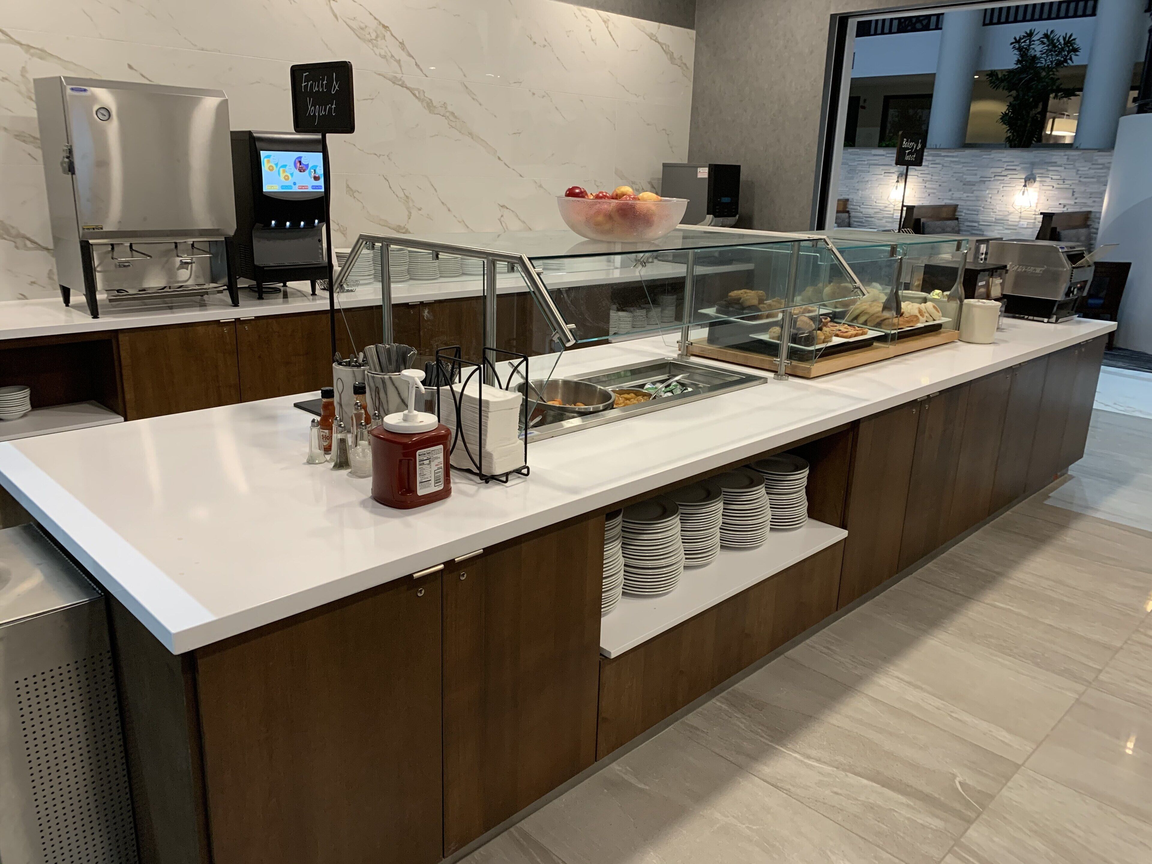 A self-service breakfast station with a marble backsplash, a fruit bowl, and a coffee machine.