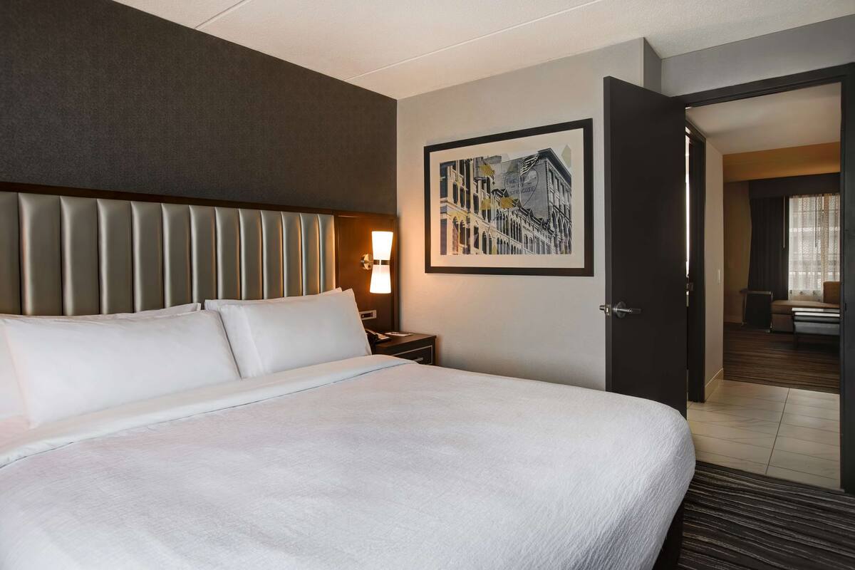 A hotel room with a large bed, a headboard, a nightstand with a lamp, and a framed picture on the wall.