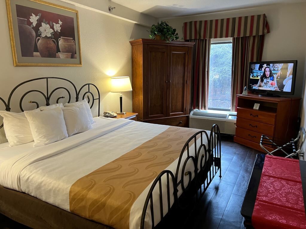 Een hotelkamer met een bed, een televisie, een kledingkast en een raam met gordijnen.
