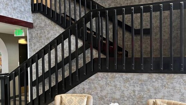 Un interior moderno con una escalera espiral negra, dos sillones color beige y una mesita redonda con una flor blanca.