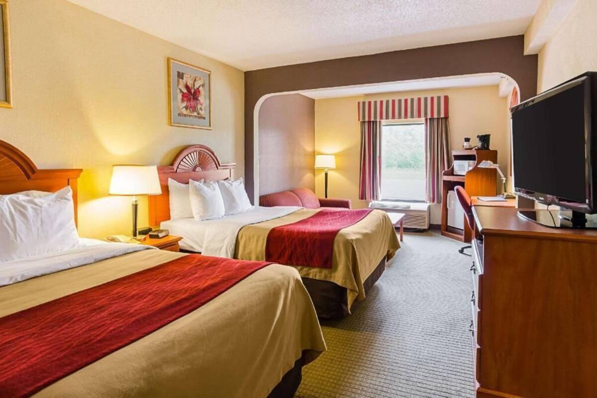 Ein Hotelzimmer mit zwei Betten, einem Schreibtisch, einem Fernseher und einem Fenster mit Vorhängen.