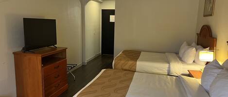 Habitación de hotel con dos camas, un televisor sobre un aparador de madera y un pasillo que conduce a otra habitación.