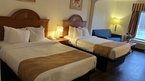 Una habitación de hotel con dos camas, un escritorio, una silla y una ventana con cortinas.