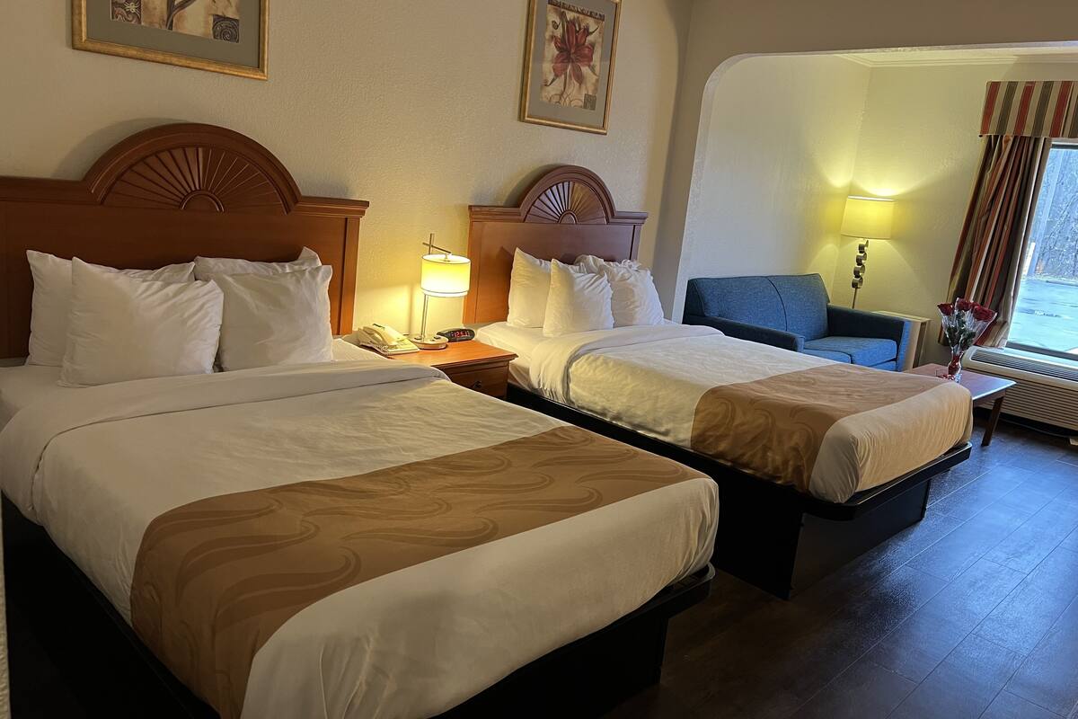Ein Hotelzimmer mit zwei Betten, einem Schreibtisch, einem Stuhl und einem Fenster mit Vorhängen.