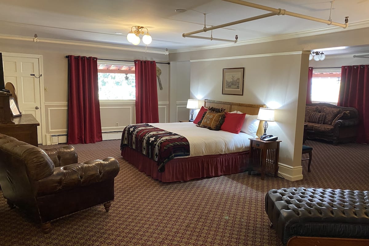 A hotel room with a large bed, two bedside tables with lamps, a leather armchair, a sofa, and a patterned carpet.