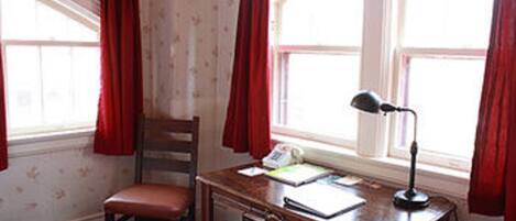 A room with a wooden desk, a chair, a lamp, and a window with red curtains.
