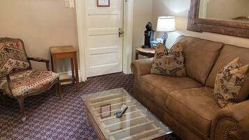 Una sala de estar con un sofá marrón, un sillón estampado y una mesa de centro de vidrio.