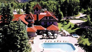 A large, multi-story building with a red roof, surrounded by lush greenery and mountains in the background.