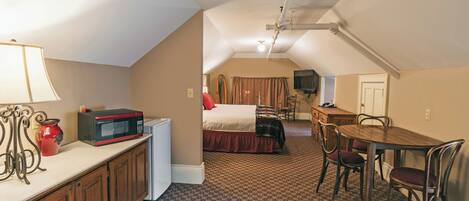 A compact hotel room with a kitchenette, a bed, a dining area, and a TV.