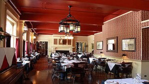 A spacious dining area with multiple tables and chairs, a chandelier, and a patterned wall.