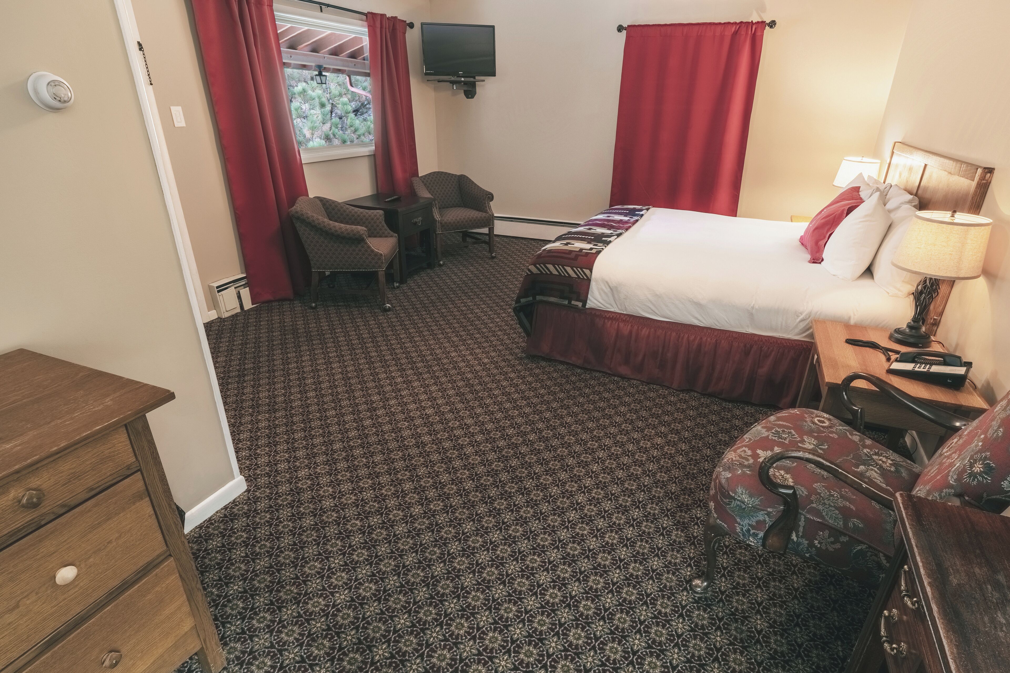 A hotel room with a bed, a desk, a chair, a TV, and a lamp.
