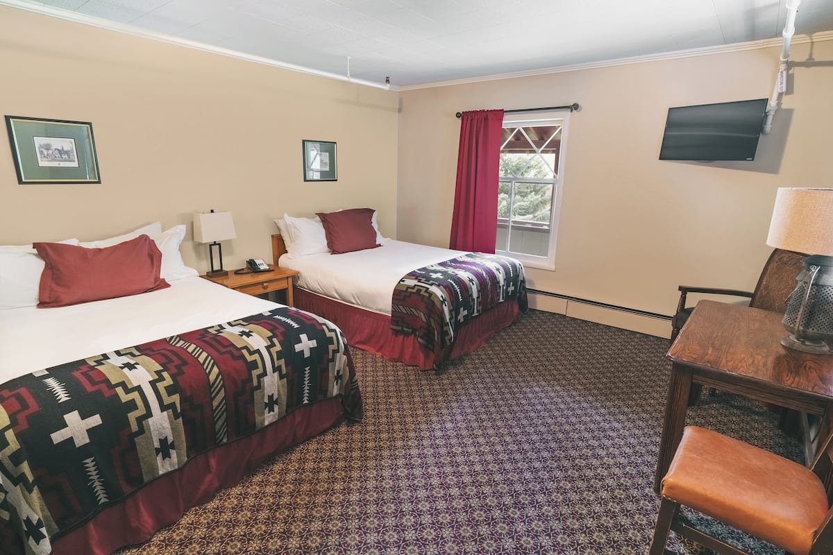 A hotel room with two beds, a TV, a desk, and a chair.