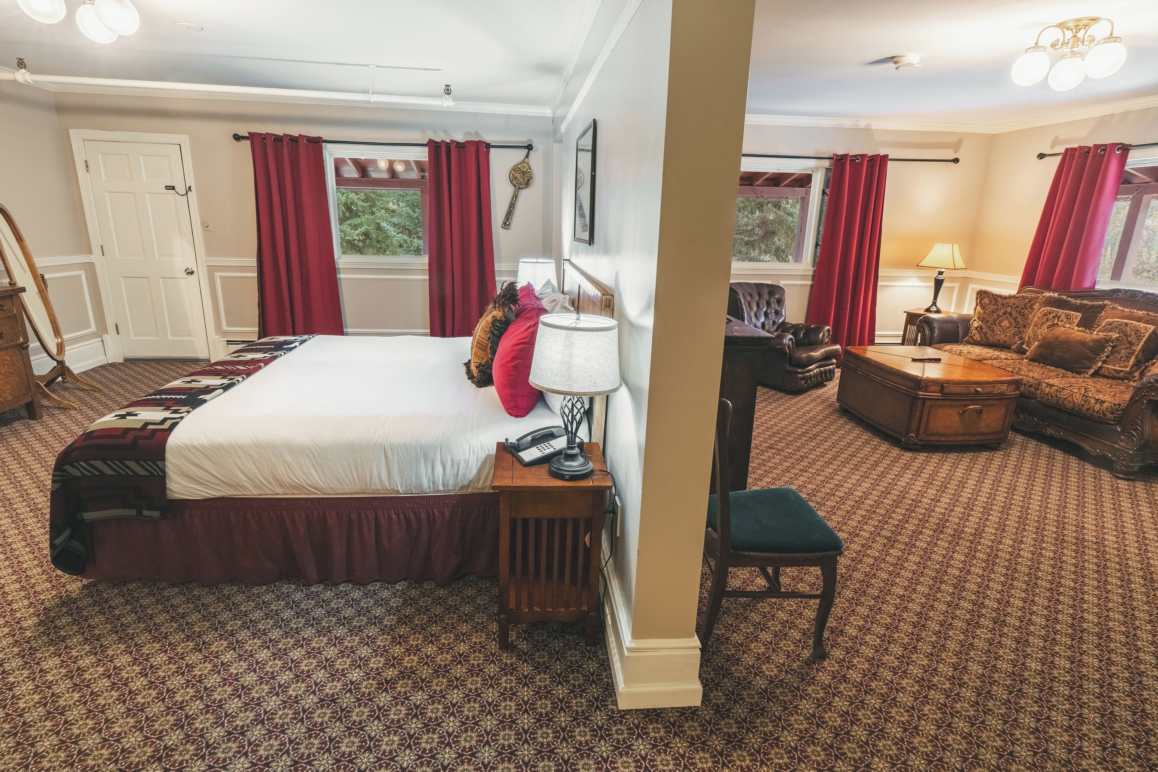 A well-furnished hotel room with a large bed, a sitting area with a sofa and armchair, a small table, and a lamp.