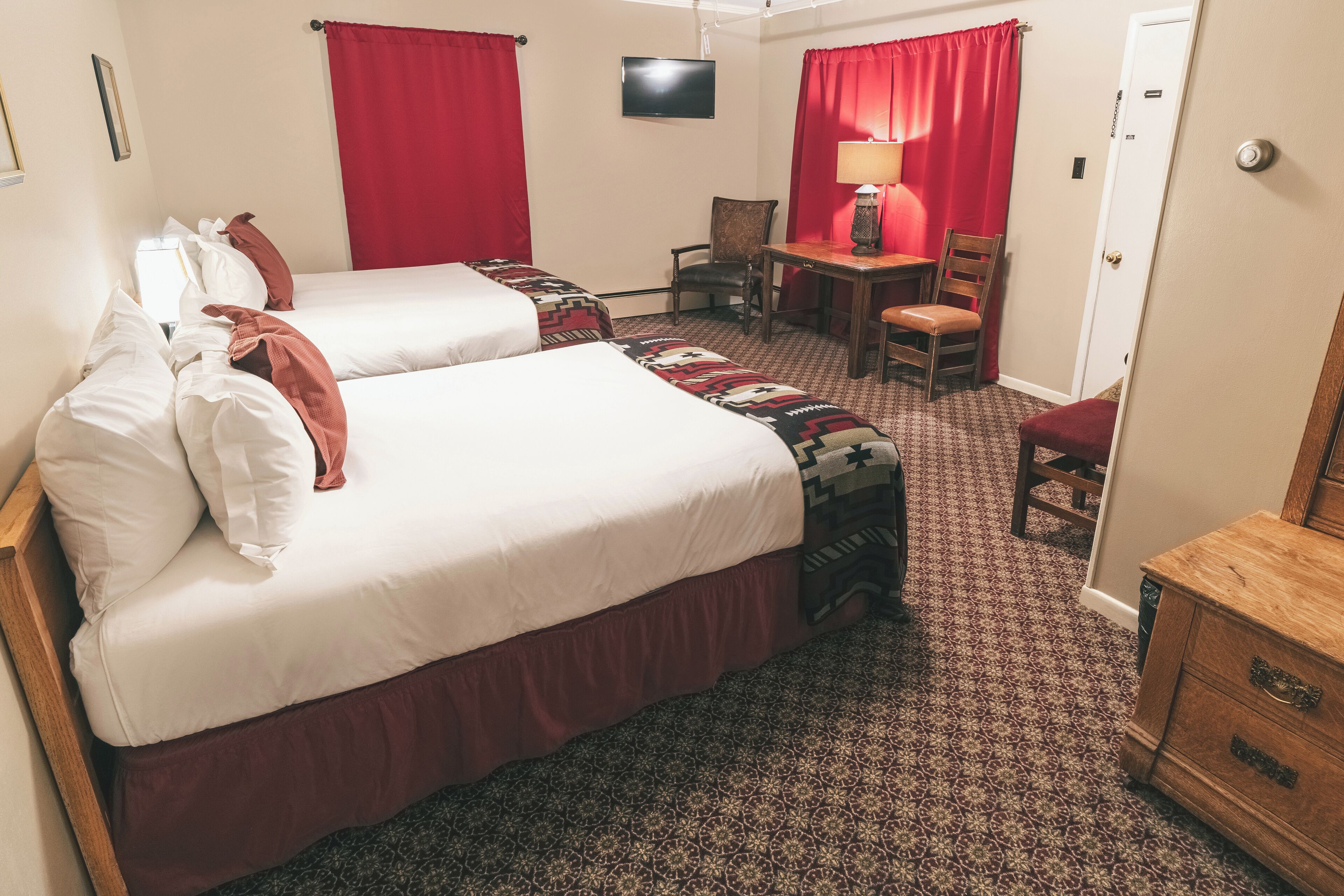 A hotel room with two beds, a desk, a chair, a TV, and a wardrobe.