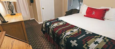 A hotel room with a bed, a desk with a lamp, a shower curtain, and a door.