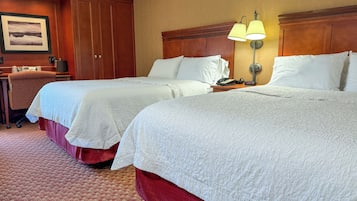 Una habitación de hotel con dos camas, un escritorio, una silla, una lámpara y un cuadro en la pared.