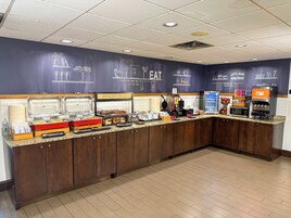 A breakfast bar with various food options, a coffee machine, and a juice dispenser.