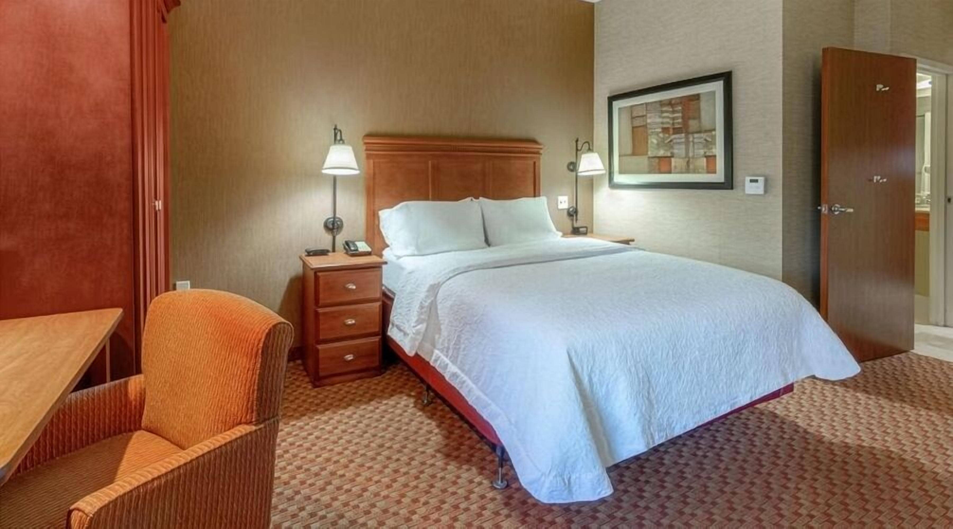 Une chambre d’hôtel comprenant un lit, une table de chevet, une chaise et une armoire.