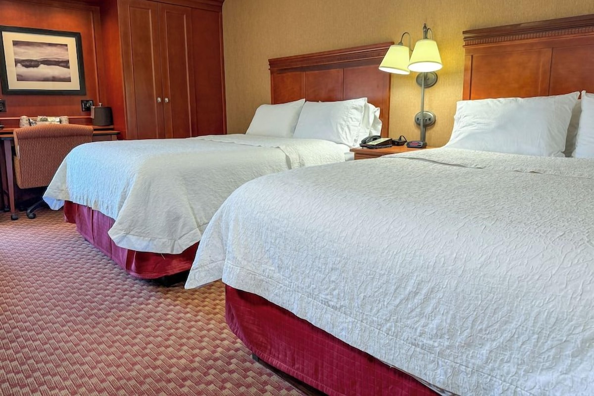 A hotel room with two beds, a desk, and a lamp.