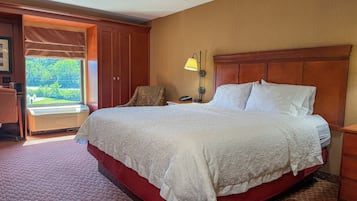 A hotel room with a large bed, a desk with a lamp, a chair, and a view of the outdoors.