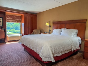 A hotel room with a large bed, a desk with a lamp, a chair, and a view of the outdoors. - Par-A-Dice Inn (East Peoria)