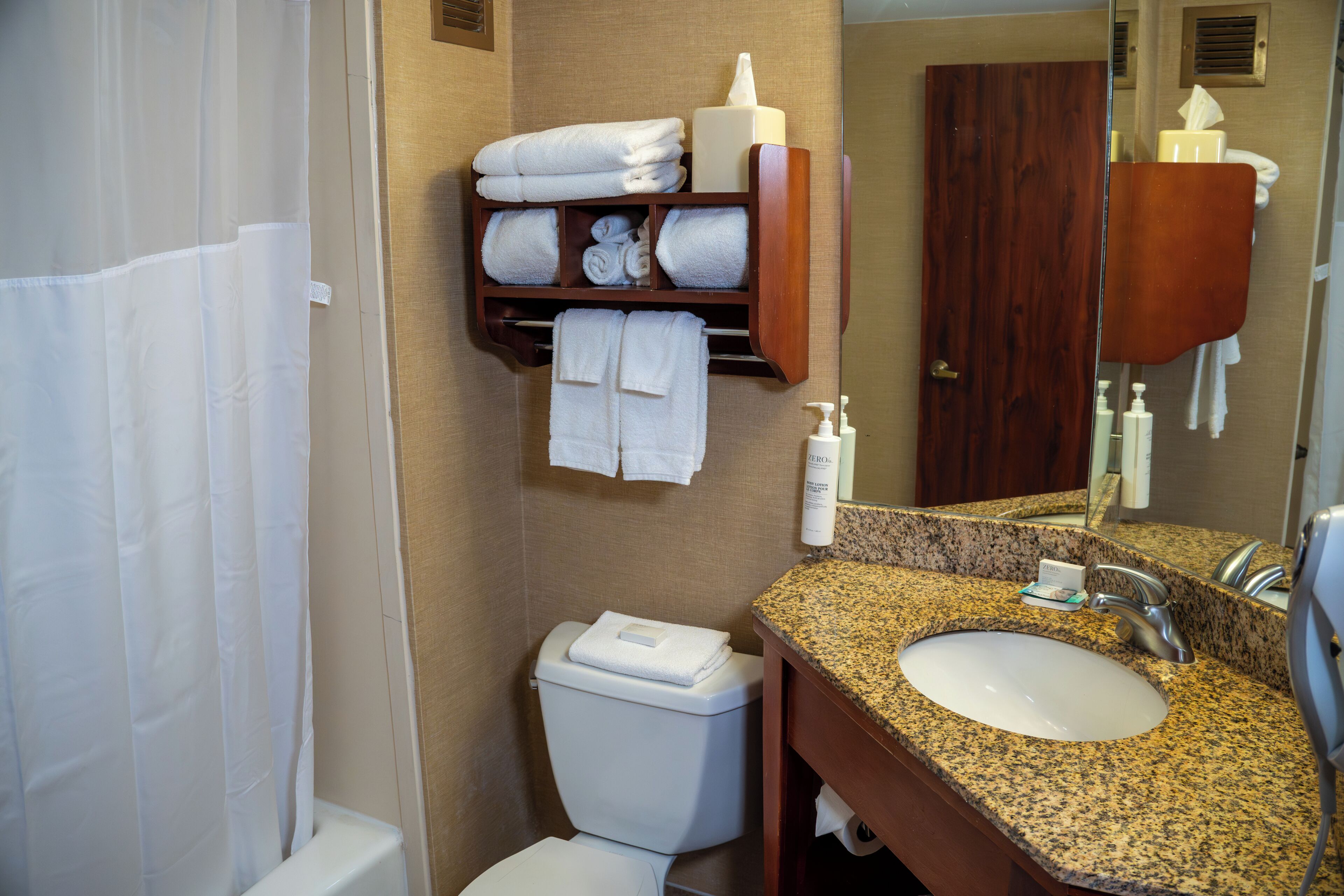 A bathroom with a white sink, a mirror, a towel rack with folded towels, and a toilet.