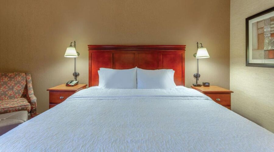 Une chambre d’hôtel avec un grand lit, deux tables de chevet avec des lampes, une chaise et un tableau encadré au mur.