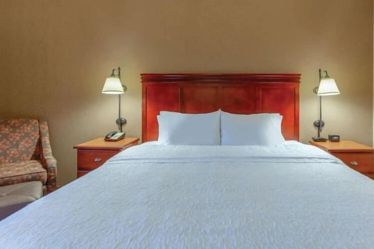 A hotel room with a large bed, two bedside tables, a chair, and a framed picture on the wall.