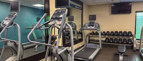 A gym with treadmills, elliptical machines, and a wall of dumbbells.